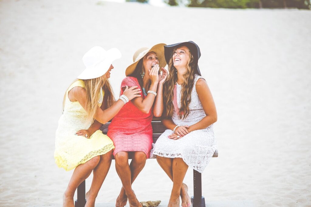 The Ultimate Guide To Planning A Girls Trip - Women in Sundresses and Hats Laughing on Beach