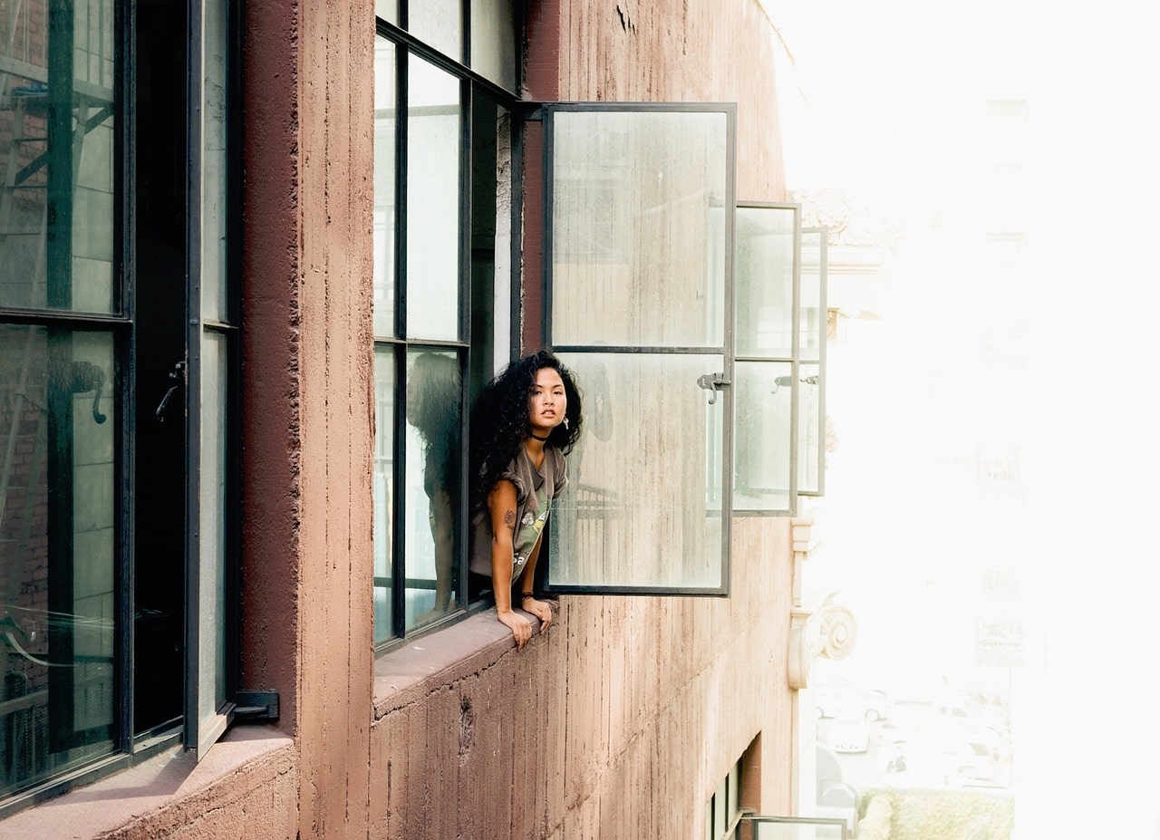 Safe and Inclusive Apartment Communities - Woman Peeking Out of Window of a Building