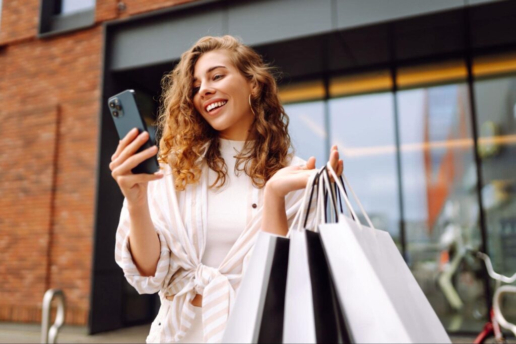 end of summer - happy woman holding phone and shopping bags